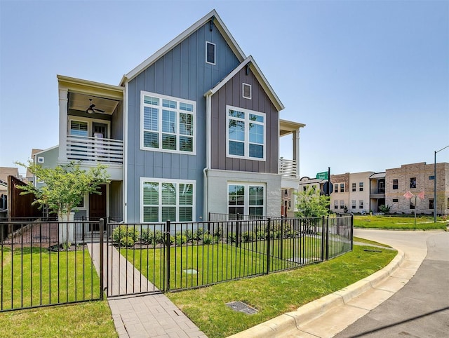 view of front facade with a fenced front yard, board and batten siding, a balcony, a front lawn, and a gate