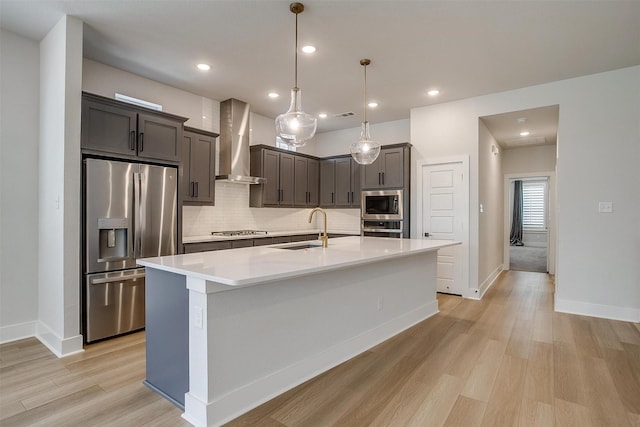 kitchen with appliances with stainless steel finishes, light wood-style flooring, wall chimney exhaust hood, decorative backsplash, and a sink