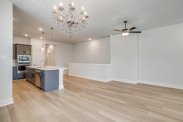 kitchen featuring ceiling fan with notable chandelier, light wood-type flooring, appliances with stainless steel finishes, light countertops, and a sink