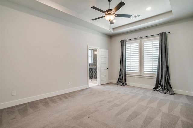 empty room featuring carpet flooring, visible vents, baseboards, and a raised ceiling