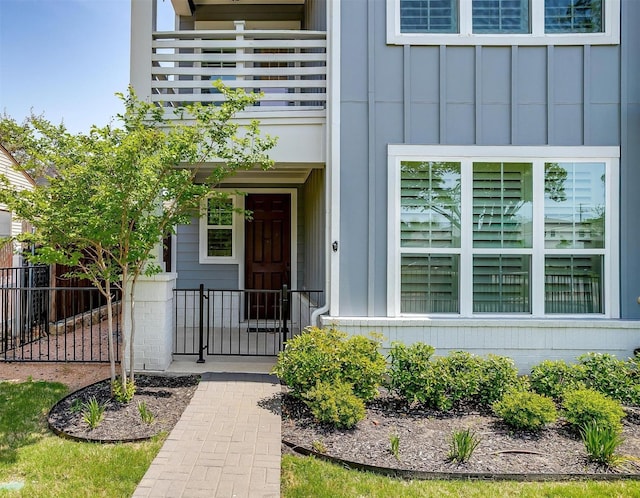 property entrance featuring a balcony, board and batten siding, and fence