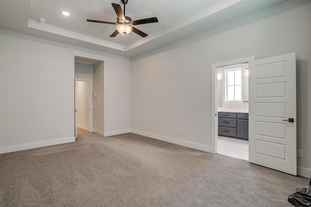 empty room with ceiling fan, a raised ceiling, light carpet, and baseboards