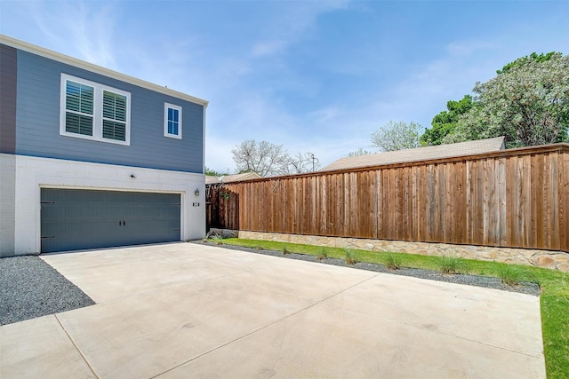view of property exterior with a garage, fence, and concrete driveway