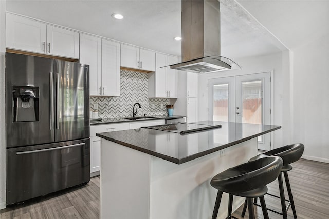 kitchen with stainless steel fridge with ice dispenser, dark countertops, island exhaust hood, light wood-style flooring, and a breakfast bar area