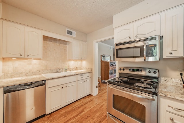 kitchen with visible vents, a sink, light wood-type flooring, appliances with stainless steel finishes, and white cabinetry