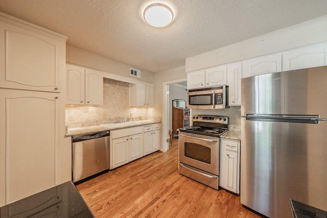 kitchen with visible vents, a textured ceiling, white cabinetry, light wood finished floors, and stainless steel appliances