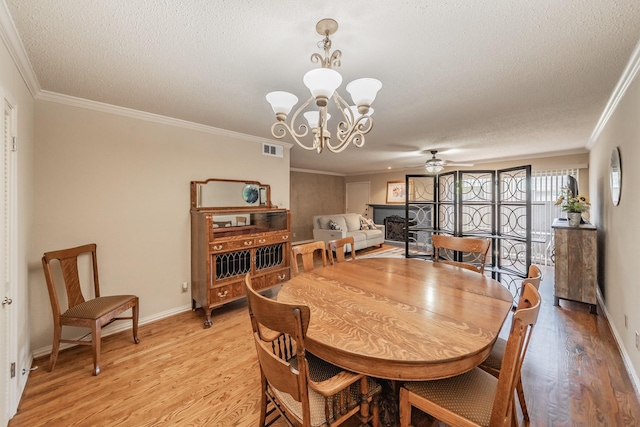 dining room featuring visible vents, ornamental molding, light wood-type flooring, a textured ceiling, and ceiling fan with notable chandelier