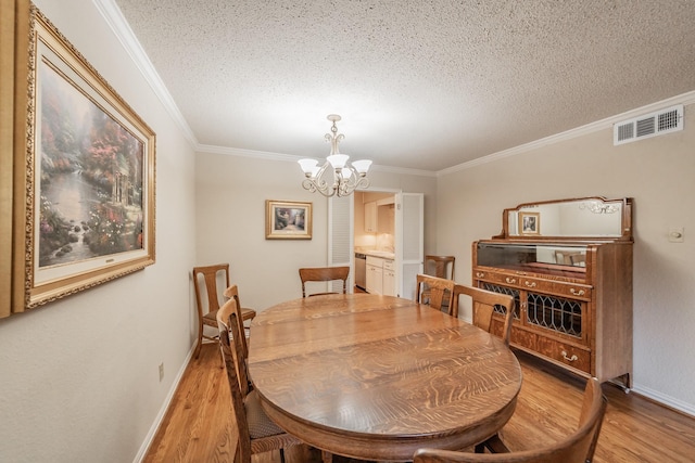 dining space featuring crown molding, a textured ceiling, an inviting chandelier, light wood-style flooring, and visible vents
