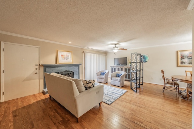 living area with a ceiling fan, ornamental molding, wood finished floors, and a textured ceiling