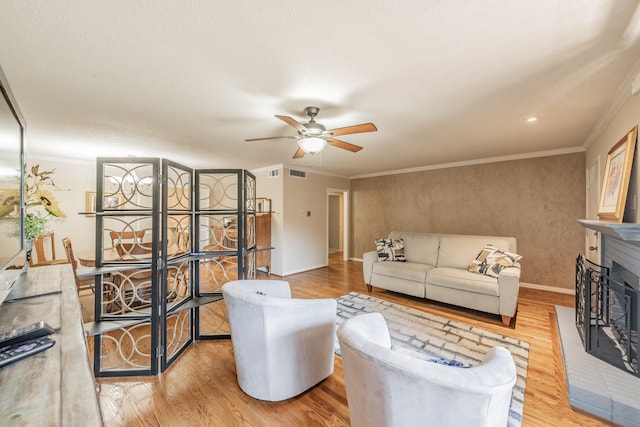 living room with light wood-type flooring, visible vents, ceiling fan, and crown molding