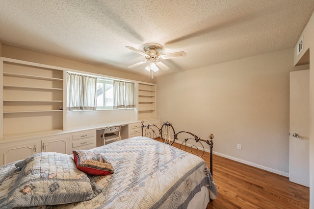 bedroom featuring wood finished floors, visible vents, a ceiling fan, baseboards, and a textured ceiling