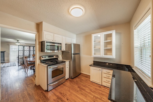 kitchen featuring glass insert cabinets, light wood-style flooring, a ceiling fan, white cabinets, and appliances with stainless steel finishes