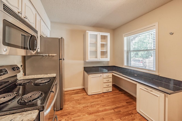 kitchen featuring built in study area, a textured ceiling, white cabinets, light wood-style floors, and appliances with stainless steel finishes