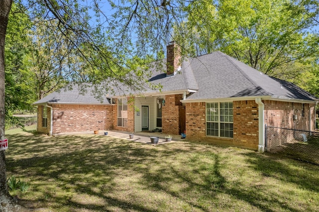 rear view of property with roof with shingles, a chimney, a patio area, brick siding, and a lawn