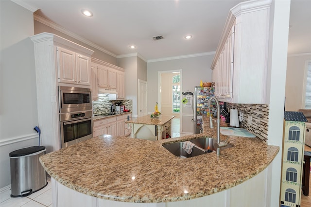 kitchen with light stone counters, a kitchen island, visible vents, appliances with stainless steel finishes, and a sink