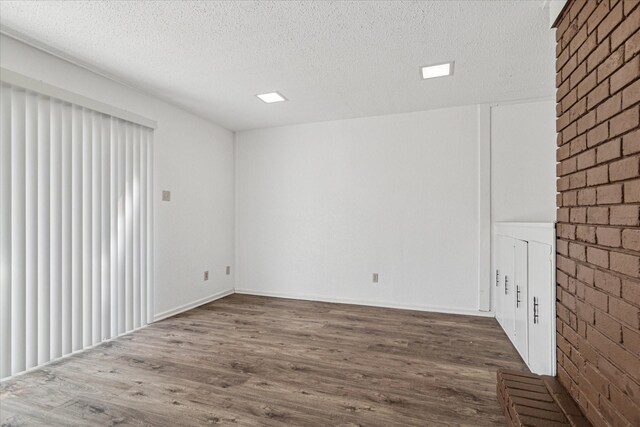 empty room featuring a textured ceiling, wood finished floors, and brick wall