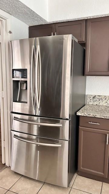 kitchen with light tile patterned floors, light stone countertops, stainless steel fridge, and dark brown cabinetry