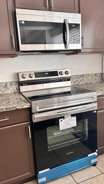 kitchen featuring dark brown cabinetry, stainless steel appliances, and light tile patterned flooring