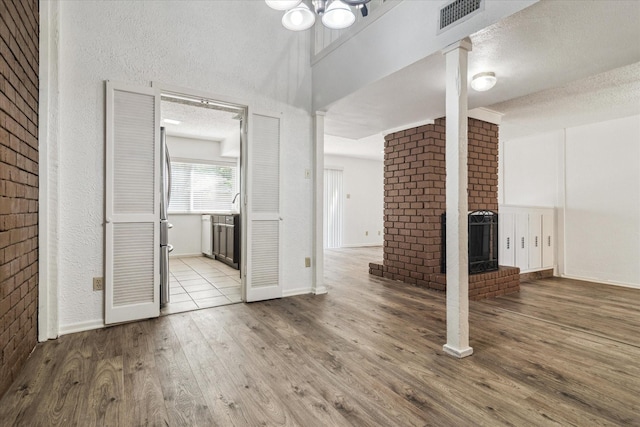 unfurnished living room with a fireplace, wood finished floors, visible vents, and a textured ceiling