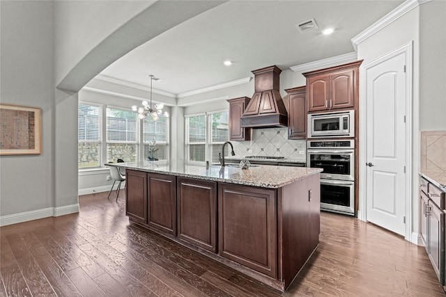 kitchen featuring visible vents, a chandelier, a kitchen island with sink, stainless steel appliances, and premium range hood