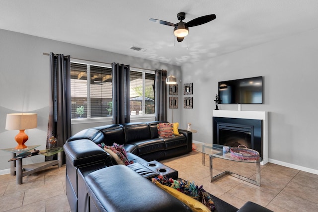 living area featuring a glass covered fireplace, baseboards, light tile patterned floors, a ceiling fan, and visible vents