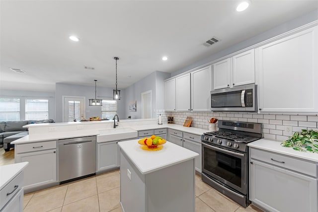 kitchen with a peninsula, open floor plan, visible vents, stainless steel appliances, and a sink