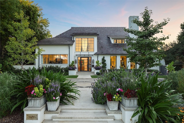 rear view of property featuring roof with shingles, stucco siding, and french doors