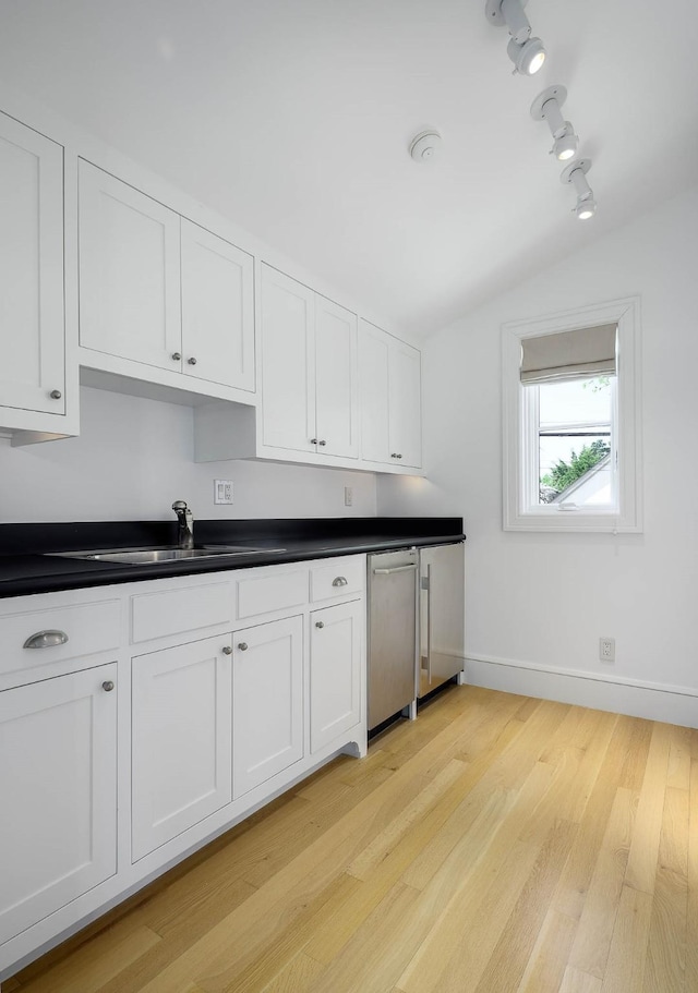 kitchen with baseboards, vaulted ceiling, white cabinetry, dishwasher, and a sink