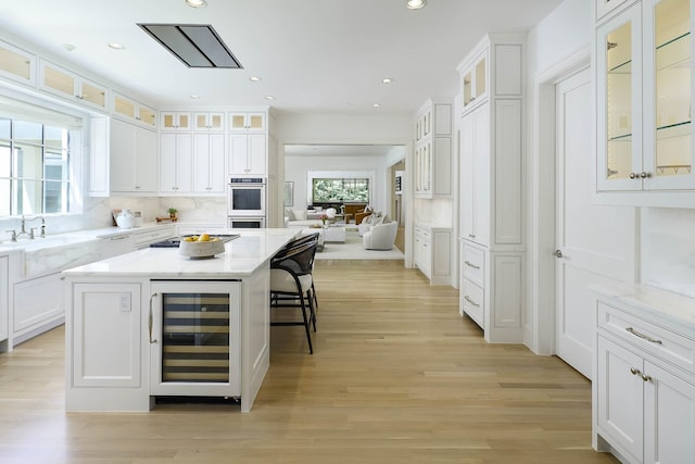 kitchen featuring white cabinets, a breakfast bar, a sink, beverage cooler, and stainless steel double oven