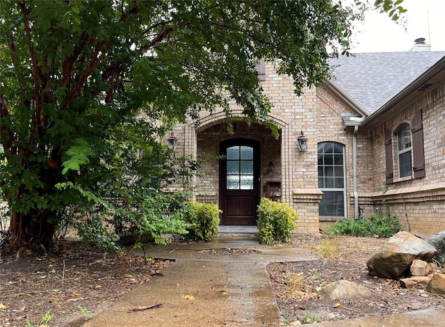 entrance to property featuring brick siding and roof with shingles
