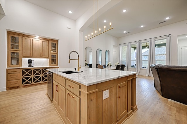 kitchen featuring light stone counters, backsplash, a kitchen island with sink, light wood-style floors, and a sink