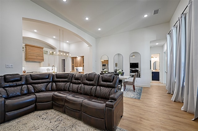 living area featuring light wood-style floors, arched walkways, visible vents, recessed lighting, and lofted ceiling