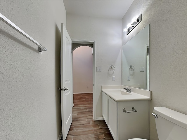 half bathroom featuring a textured wall, toilet, vanity, and wood finish floors