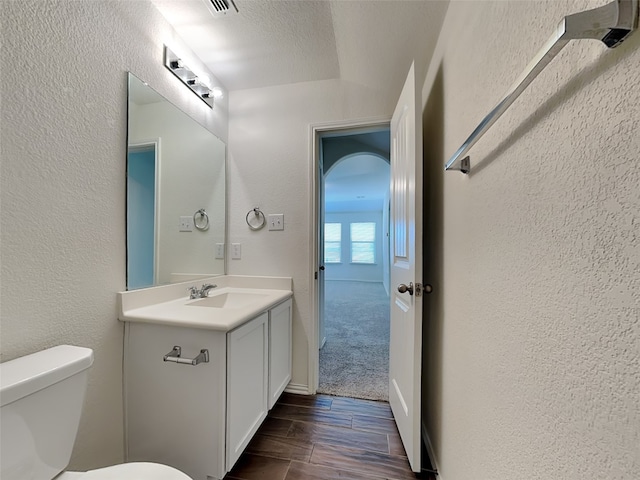 half bathroom with a textured wall, vanity, toilet, and wood finished floors