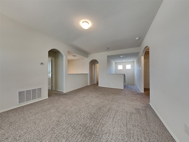 spare room featuring light carpet, arched walkways, visible vents, and baseboards