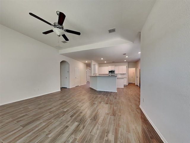 unfurnished living room with ceiling fan, light wood-type flooring, arched walkways, visible vents, and baseboards