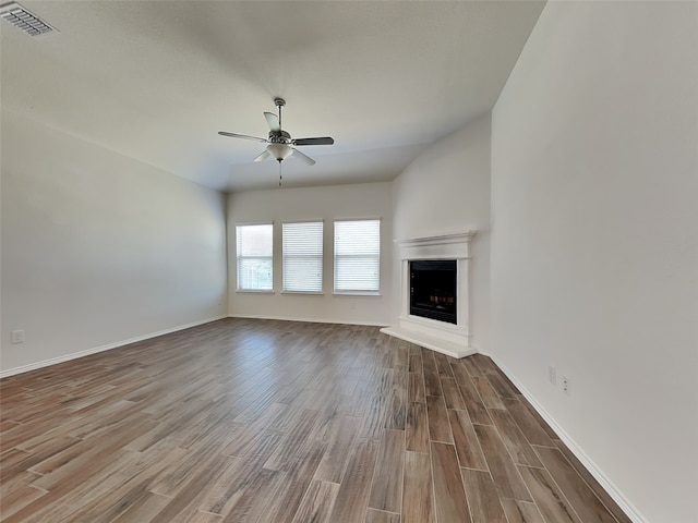 unfurnished living room with visible vents, baseboards, a fireplace with raised hearth, a ceiling fan, and wood finished floors