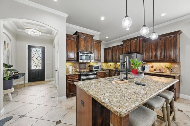 kitchen with light tile patterned floors, arched walkways, a sink, appliances with stainless steel finishes, and light stone countertops