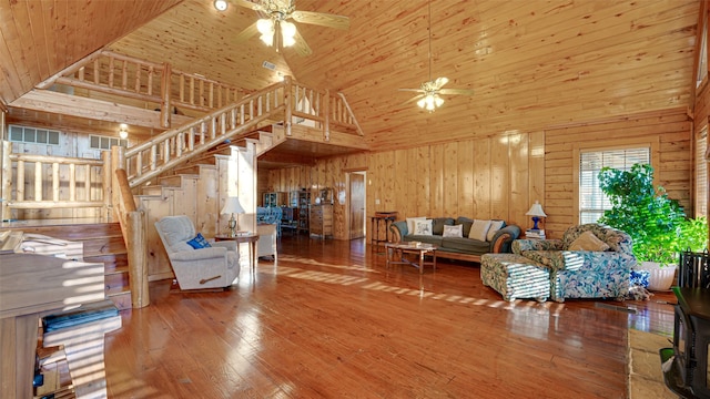 living room featuring a ceiling fan, wood walls, stairs, high vaulted ceiling, and wood-type flooring