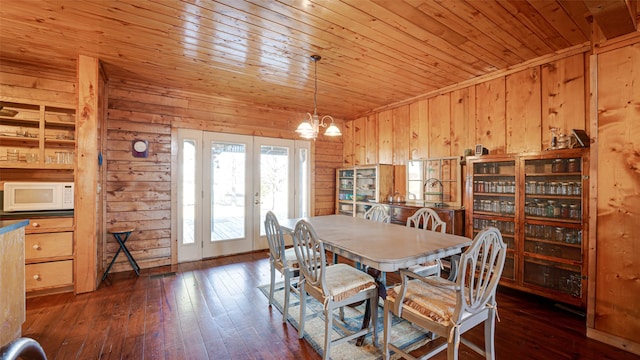 dining area featuring an inviting chandelier, french doors, wood walls, dark wood-type flooring, and wooden ceiling