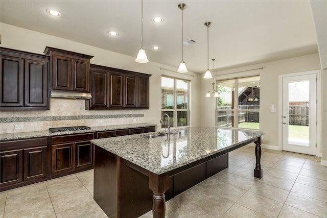 kitchen featuring stainless steel gas stovetop, under cabinet range hood, light tile patterned floors, a sink, and tasteful backsplash