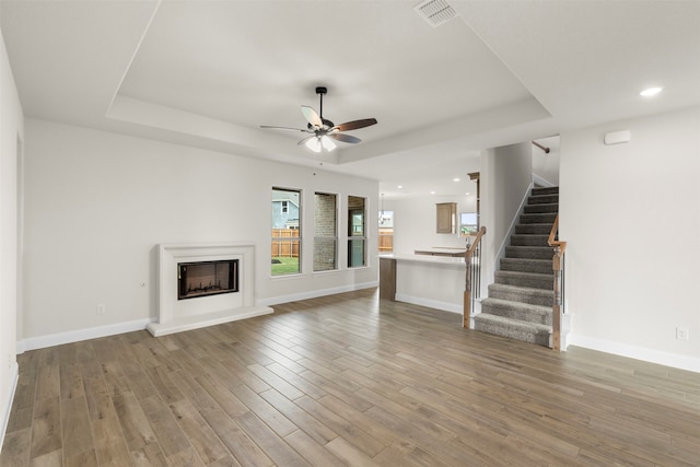 unfurnished living room featuring stairway, visible vents, a ceiling fan, and a raised ceiling