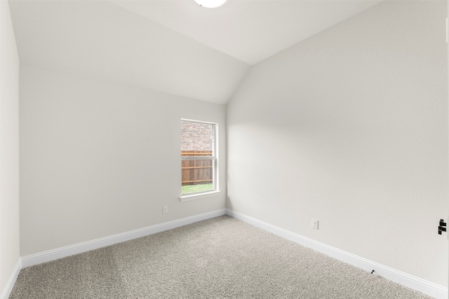 spare room featuring carpet, baseboards, and lofted ceiling