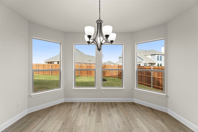unfurnished dining area featuring a chandelier, light wood finished floors, and baseboards