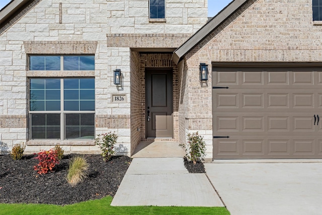 view of exterior entry featuring brick siding, an attached garage, and driveway