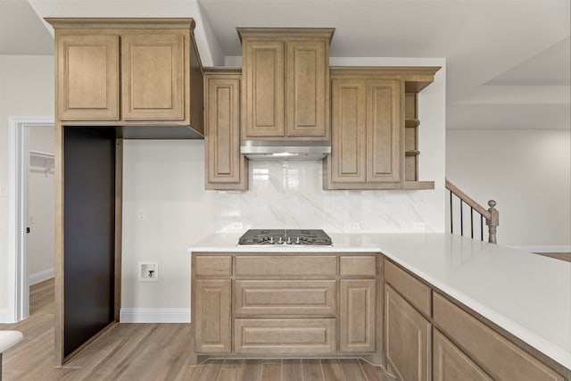 kitchen with open shelves, under cabinet range hood, light wood-style flooring, stainless steel gas cooktop, and decorative backsplash