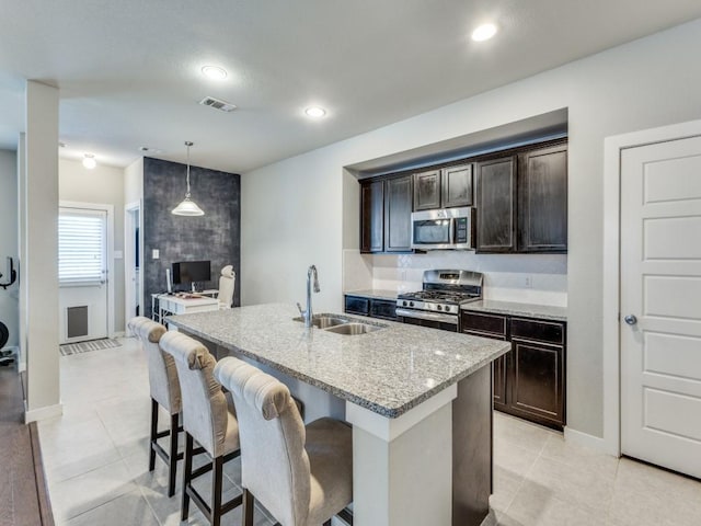1116 Fulbourne Dr, Anna, TX 75409 - kitchen featuring appliances with stainless steel finishes, a sink, light stone countertops, an island with sink, and dark brown cabinetry