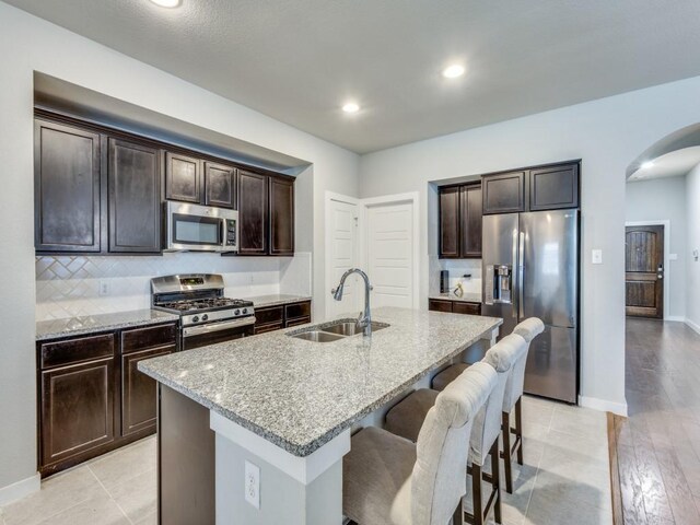 1116 Fulbourne Dr, Anna, TX 75409 - kitchen with appliances with stainless steel finishes, a sink, arched walkways, light stone countertops, and a breakfast bar area