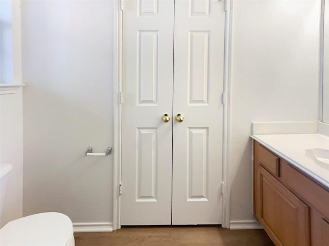 half bathroom featuring toilet, vanity, wood finished floors, and baseboards
