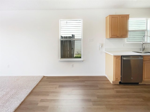 kitchen featuring baseboards, light countertops, stainless steel dishwasher, light wood finished floors, and a sink